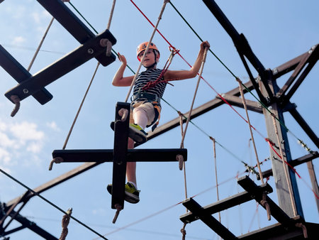 a teenage boy climbing in outdoor rope park passing obstacle course.