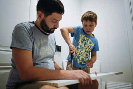An eight-year-old boy is helping his father assemble a new piece of furniture. he holds a...