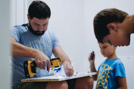 man assembling a new furniture with a screwdriver. children helping him