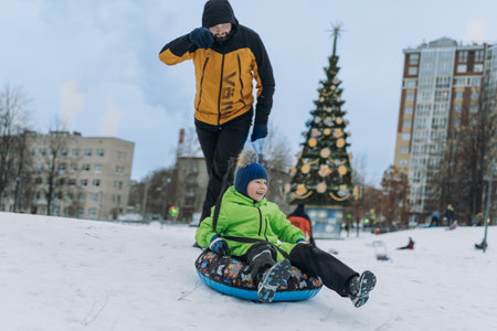 father and boy sliding down the slope in park. Winter family activities concept.の写真素材