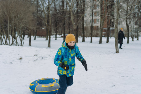 boy running with snow tubing in park. Winter family activities concept.の写真素材