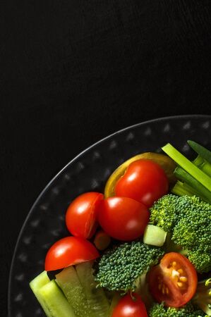 Vegetable salad. Broccoli, tomatoes, cucumbers, green onions on a black wooden background. Place the text at the top left. The view from the top.の写真素材