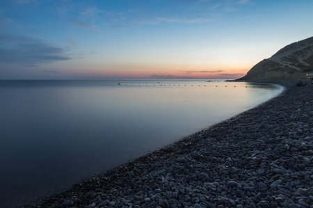 Long exposure. Evening on the beach under the blue sky. The coastline is curved, the mountain in the...
