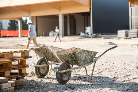 Two wheelbarrows in front of a construction site for small business premises. Property construction, small scale enterprise, expanding property concept.のeditorial素材