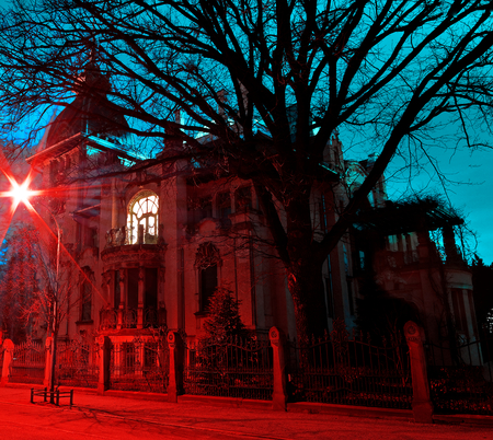 Gloomy haunted house with red and light blue illuminated by a street lamp at nightの写真素材