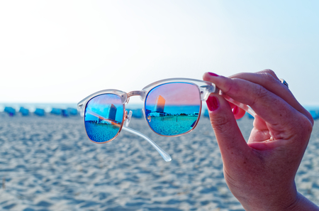 Sunglasses with the Hotel Neptune in Warnem?nde in the background on the beach in the sunshine held by one handの写真素材