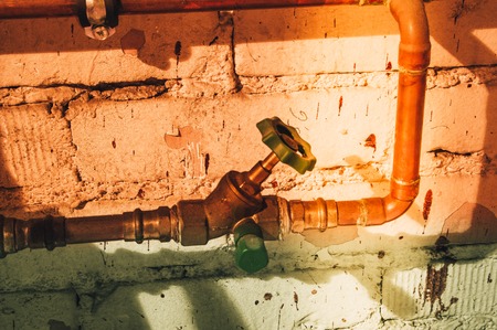 Copper faucet with copper pipe and water pipe in front of a masonryの写真素材