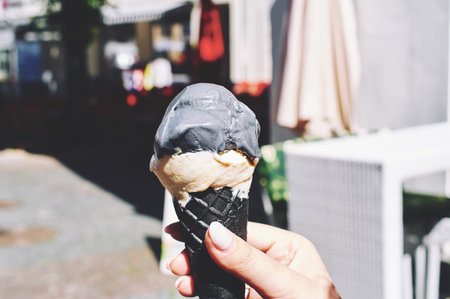 Hand holding a black ice cream cone with gray ice with activated carbon