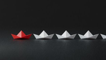 Leadership concept with red paper ship leading white ones on black background