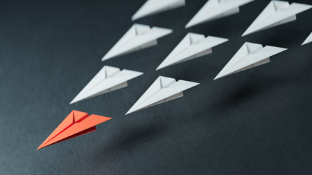Leadership concept with red paper plane leading among white ones on dark background