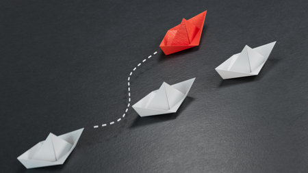group of black paper boats are sailing in one direction, one red is sailing in the opposite direction. The concept of an extraordinary personality, to act contrary to the foundations of societyの写真素材