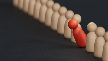 Red wooden figure stepping out from a line of beige figures, illustrating different thinking and leading change. A concept of uniqueness and standing out. 3D rendering on black background.の写真素材