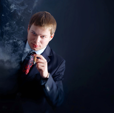 The man smoke a cigar. lots of smoke. A dark backgroundの写真素材