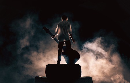 The musician plays on a large rock guitar in a great smoke