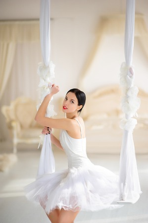 Beauty brunette ballerina on a swing in room, with ballet skirt and corsetの写真素材