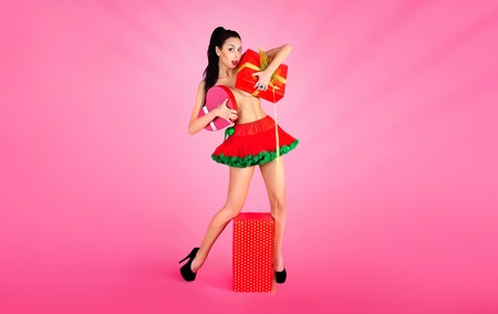 Joyful naked girl in red skirt, having fun emotionally enjoying holding gift boxes on red background.  Valentine day.の写真素材