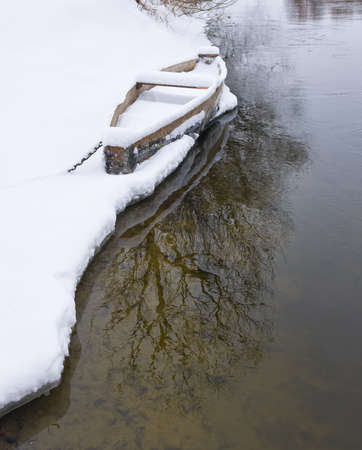 Wood boat covered with snow on the shore of winter riverの写真素材