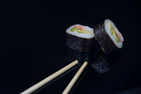 two pieces of sushi with chopsticks in dark backgroundの写真素材