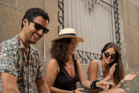 a group of three friends having fun and laughing on a bench in the streetの写真素材