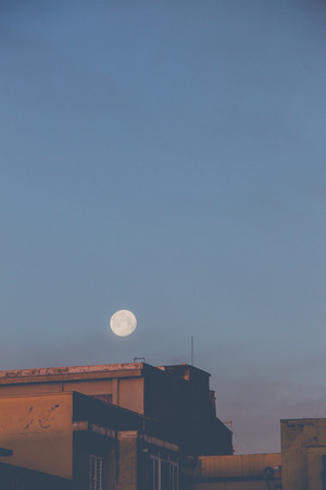 First lights of the day. The moon still in the sky above old buildings in a district of Bari. Balconies, verandas and windows still closed, people still sleep.のeditorial素材