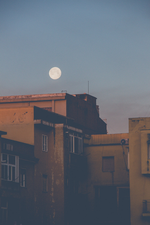 First lights of the day. The moon still in the sky above old buildings in a district of Bari. Balconies, verandas and windows still closed, people still sleep.の写真素材