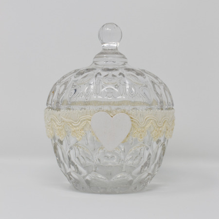 A glass container and lid, decorated by a handmade ribbon and a white wooden heart as an ornament.の写真素材
