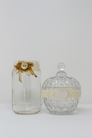 A glass bottle, container and lid, decorated with handmade ribbons and ornaments like a button and a white wooden heart.の写真素材