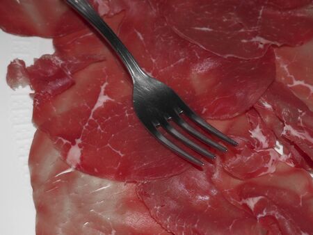 Appetizer on the table for lunch time. Sliced bresaola on a white plate and fork photographed with the partial color art filter on camera.の写真素材