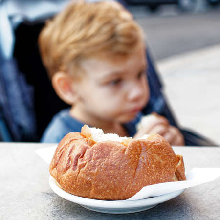 Bari, Italy - 09 06 2020: A morning with the family to have breakfast in a bar in the city. A baby sitting in a stroller eats a croissant served on a white plate.のeditorial素材