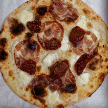 Dinner time with a typical food of Italian cuisine. A traditional pizza with mozzarella and the addition of dried tomatoes and ham.の写真素材