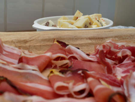 Preparing a dinner for a birthday party with guests in the house. Sliced ham served on a wooden tray and pieces of cheese on a plate.の写真素材