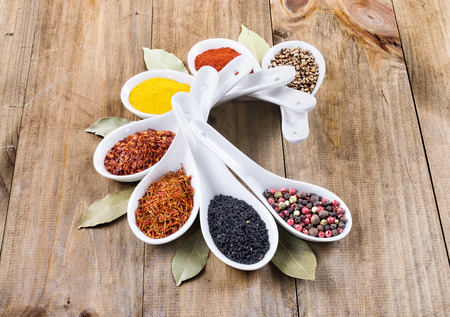 Assortment of spices in white spoons, on wooden backgroundの写真素材