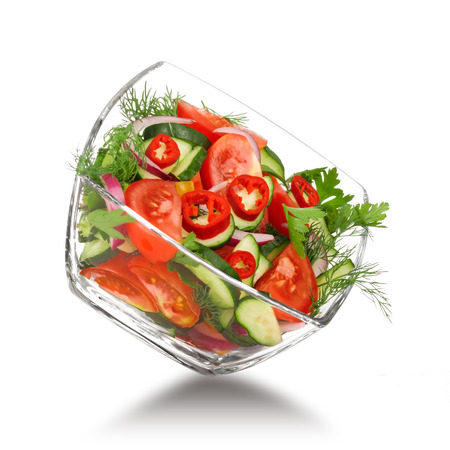 glass salad bowl in flight with vegetables: tomato, pepper, cucumber, onion, dill and parsley. Isolated on white backgroundの写真素材