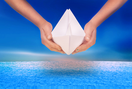 hand holding a paper boat on a sea backgroundの写真素材