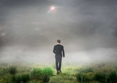 The concept of the unknown. Man in suit walk in fog on grass field. Concept of search the way.の写真素材