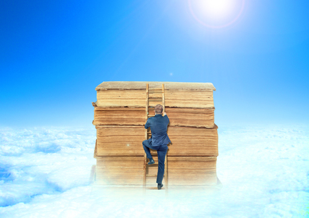 The concept of learning. A man in a suit climbs the stairs into a pile of books against the sky. The concept of enlightenment.の写真素材
