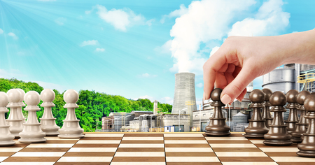 Ð¡oncept of confrontation. Female hand playing chess on factory and forest backgroundの写真素材