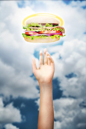 Hand reaching for a hamburger against the skyの写真素材