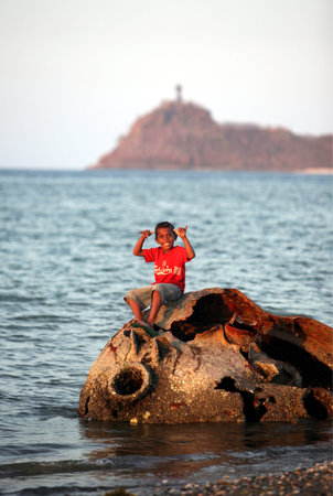 A boy on an ancient rusted and stranded boat on the beach city of Dili the capital of East Timor on the island of Timor separated into two in Asiaのeditorial素材
