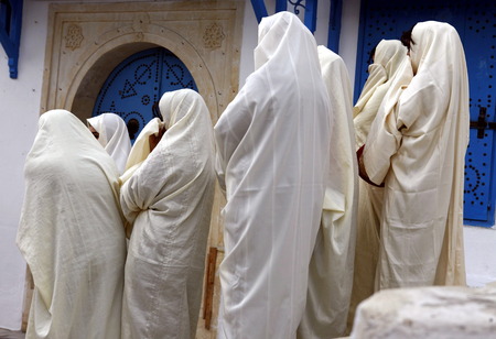 Young women in traditional white veil in the old town of Sidi Bou Said in the twilight on the Mediterranean and North of the Tunisian capital, Tunisのeditorial素材