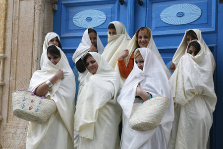 Young women in traditional white veil in the old town of Sidi Bou Said in the twilight on the Mediterranean and North of the Tunisian capital, Tunisのeditorial素材