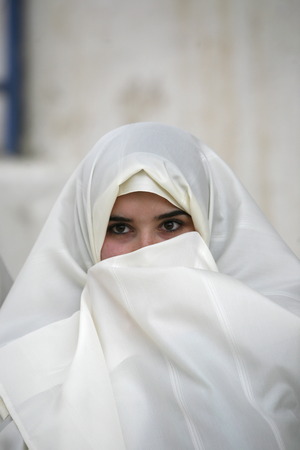 Young women in traditional white veil in the old town of Sidi Bou Said in the twilight on the Mediterranean and North of the Tunisian capital, Tunisのeditorial素材