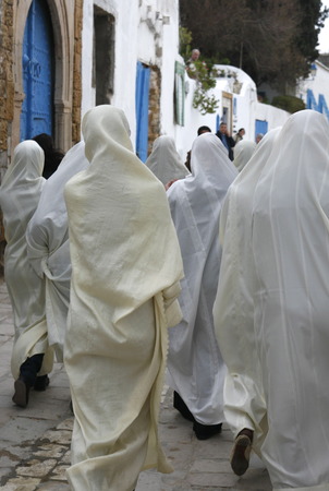 Young women in traditional white veil in the old town of Sidi Bou Said in the twilight on the Mediterranean and North of the Tunisian capital, Tunisのeditorial素材