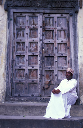 a local Men at a traditional Wood Door in the Old Town of Stone Town on the Island of Zanzibar in Tanzania.  Tanzania, Zanzibar, Stone Town, October, 2004のeditorial素材