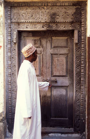 a local Men at a traditional Wood Door in the Old Town of Stone Town on the Island of Zanzibar in Tanzania.  Tanzania, Zanzibar, Stone Town, October, 2004のeditorial素材