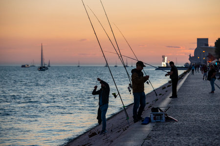 fishermen by sunset at the promenade with the monument of Discoveries or Pedaro dos Descobrimentos...
