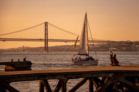 Sailboat with the Ponte 25 de Abril or 25the April Bridge at the Rio Tejo near the City of Lisbon in Portugal.  Portugal, Lisbon, October, 2021のeditorial素材