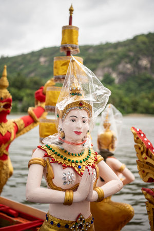 a figure is covered by plastic bag against rainshower on a decorated traditional longboat on Lake...