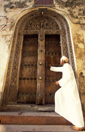 a local Men at a traditional Wood Door in the Old Town of Stone Town on the Island of Zanzibar in Tanzania.  Tanzania, Zanzibar, Stone Town, October, 2004のeditorial素材