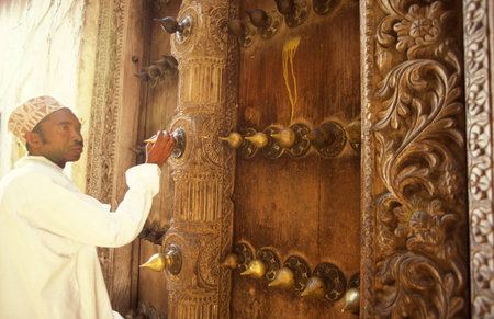 a local Men at a traditional Wood Door in the Old Town of Stone Town on the Island of Zanzibar in Tanzania.  Tanzania, Zanzibar, Stone Town, October, 2004のeditorial素材